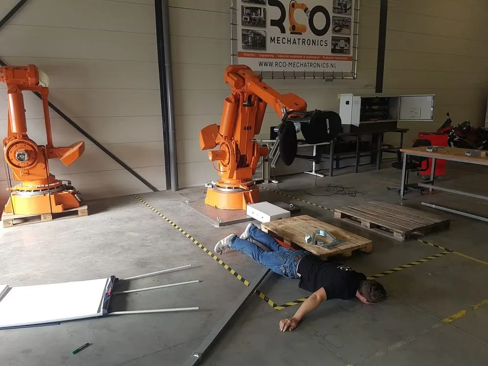 Monteur op de grond bij industriële oranje robots.