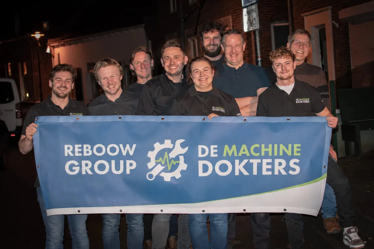 Het team houdt een banner vast met REBOOW GROUP en DE MACHINEDOKTERS erop.