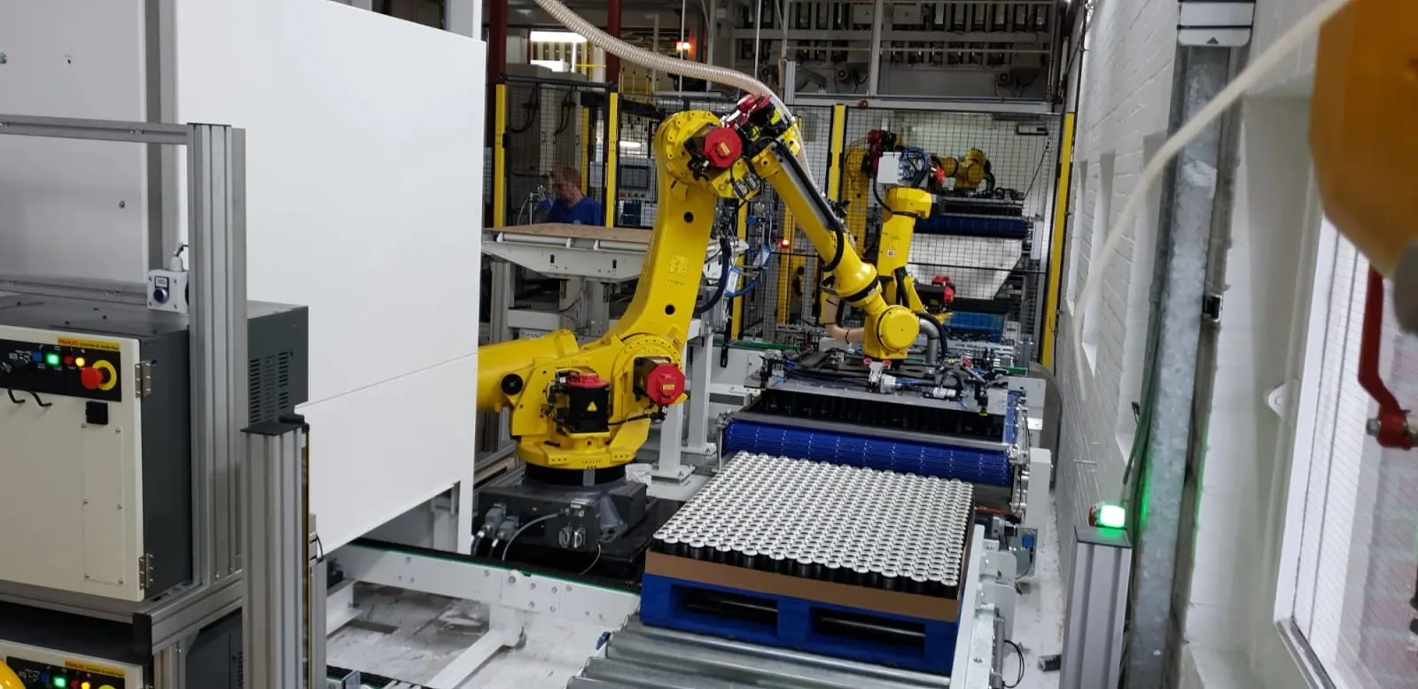 Twee FANUC-robots stapelen lagen aluminium blikjes op een pallet.