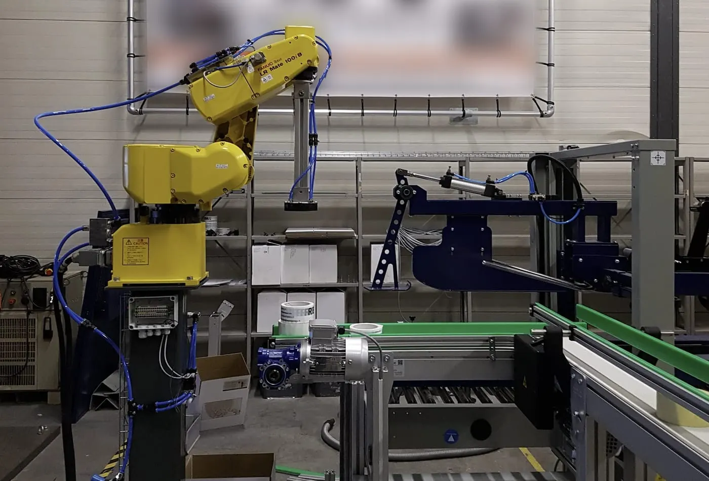 FANUC LR Mate-robot naast een transportband in een werkplaats.